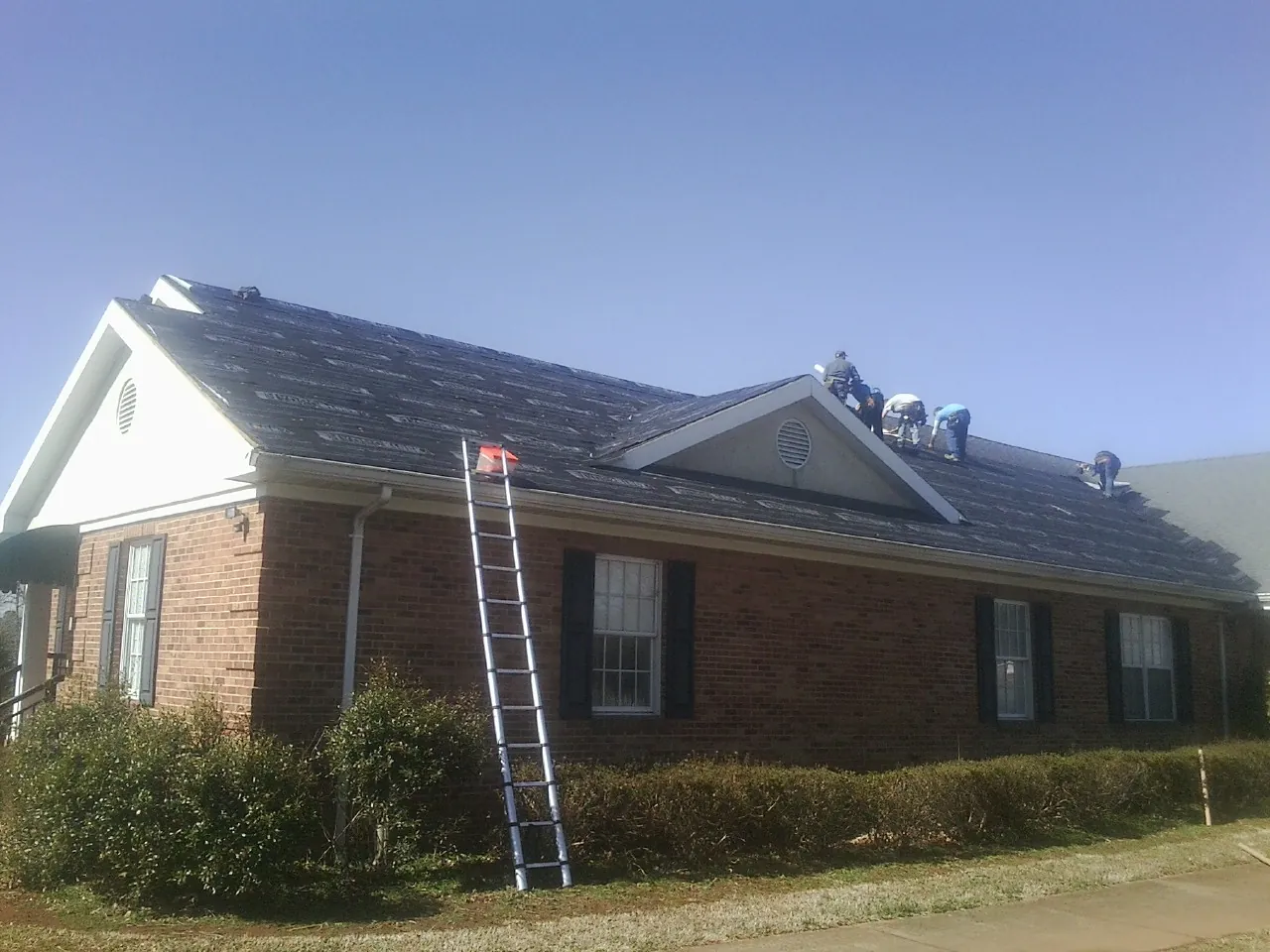 Crew tearing shingles off a brick ranch roof with a ladder set — Emergency Roof Repair work by our crew in Sharps