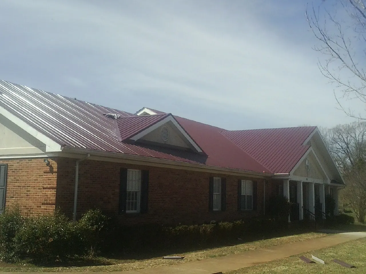 Red metal roof with gabled entries on a long brick building, from a Hail Damage Roof Repair job in Sharps
