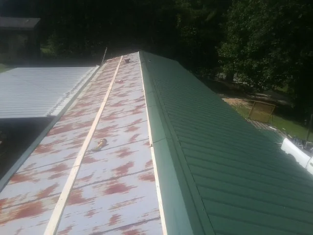 Old rusted panels beside newly installed green metal roofing — Wind Damage Roof Repair by Roofing Brothers in Sharps