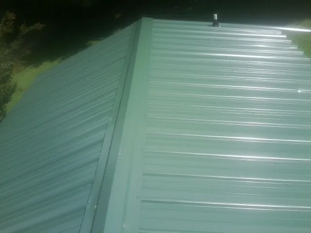 New green metal panels meeting at the ridge of a roof — Flat Roof Repair work by our crew in Sharps