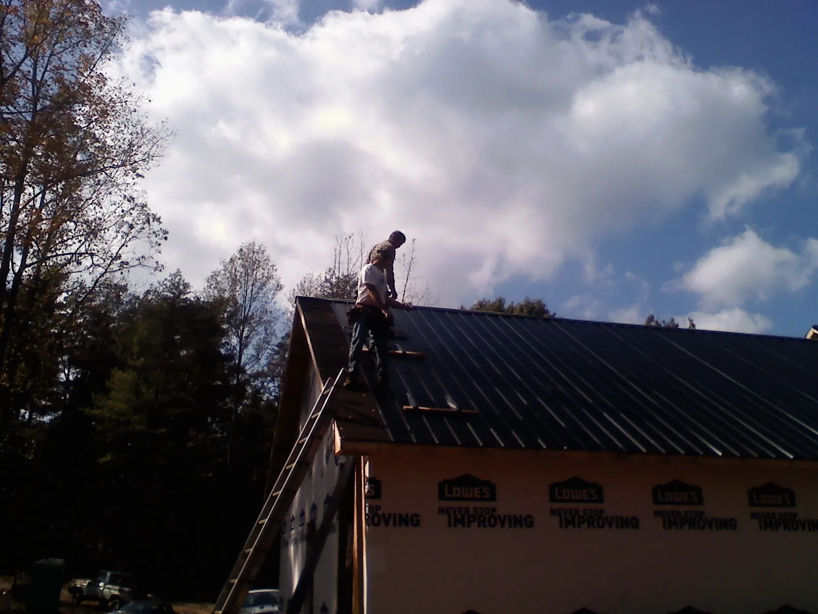 Roofer fastening dark metal panels high against a cloudy sky, from a Roof Inspection job in Sharps