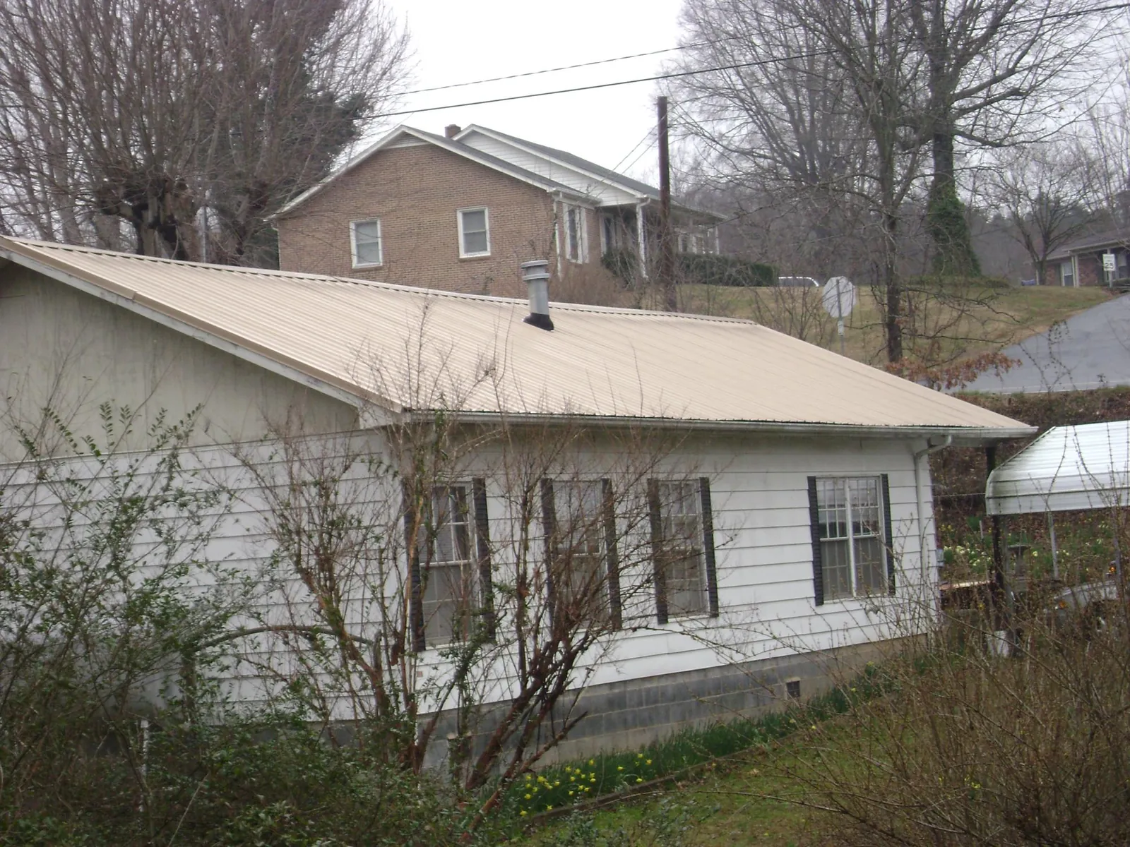 Tan metal roof on a white sided house set into a hillside — Commercial Roofing by Roofing Brothers in Sharps