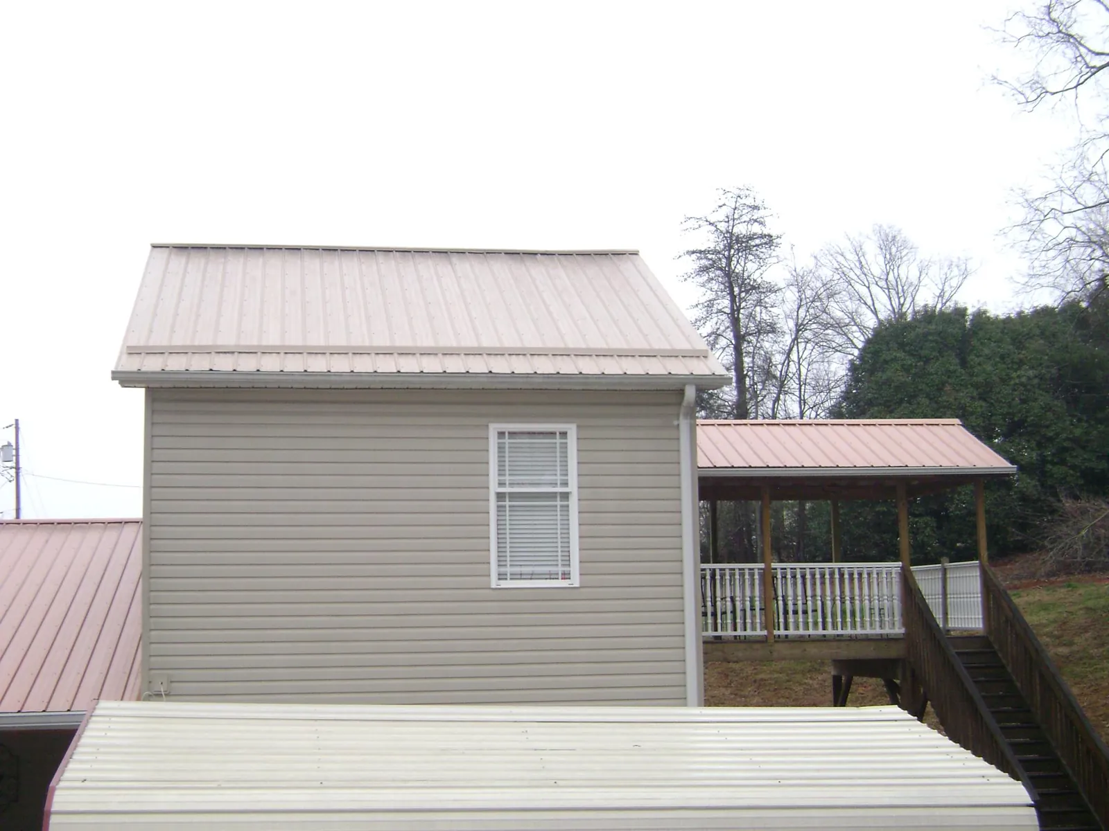 Tan metal roofs on a two story addition and attached porch, from a Roof Replacement job in Sharps